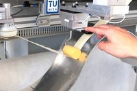Eine Hand bedient ein Maschine mit TU Wien Signet.