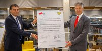 Zwei Männer halten ein gemeinsam signiertes Plakat in die Höhe