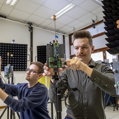 Zwei Männer schrauben mit Antennen und Platinen ausgestattete Geräte zusammen.