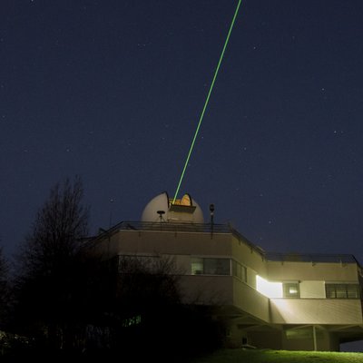 Vom Dach eines Gebäudes aus ist ein Laserlichtstrahl in den Nachthimmel gerichtet.