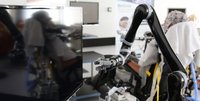 Robotischer Arm neben einem Fernseher, dahinter ein Proband mit EEG-Haube