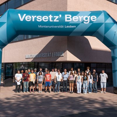 Gruppe vor dem Uni-Gebäude unter einem großen aufblasbaren Torbogen „Versetz’ Berge“ der Montanuniversität Leoben.