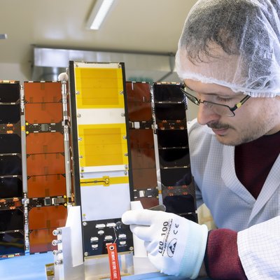 Mann mit Labormantel und Haarnetz hantiert an einem Kubus mit ausgeklappten Seitenteilen.
