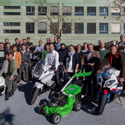 Eine Gruppe Menschen, links ein Mann mit handgeführtem Betonschleifer, mittig Personal Mobility Fahrzeuge und rechts ein Rasenmäher 