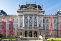Drei Fahnen wehen an Masten vor einem dreistöckigen, historischen Gebäude.
