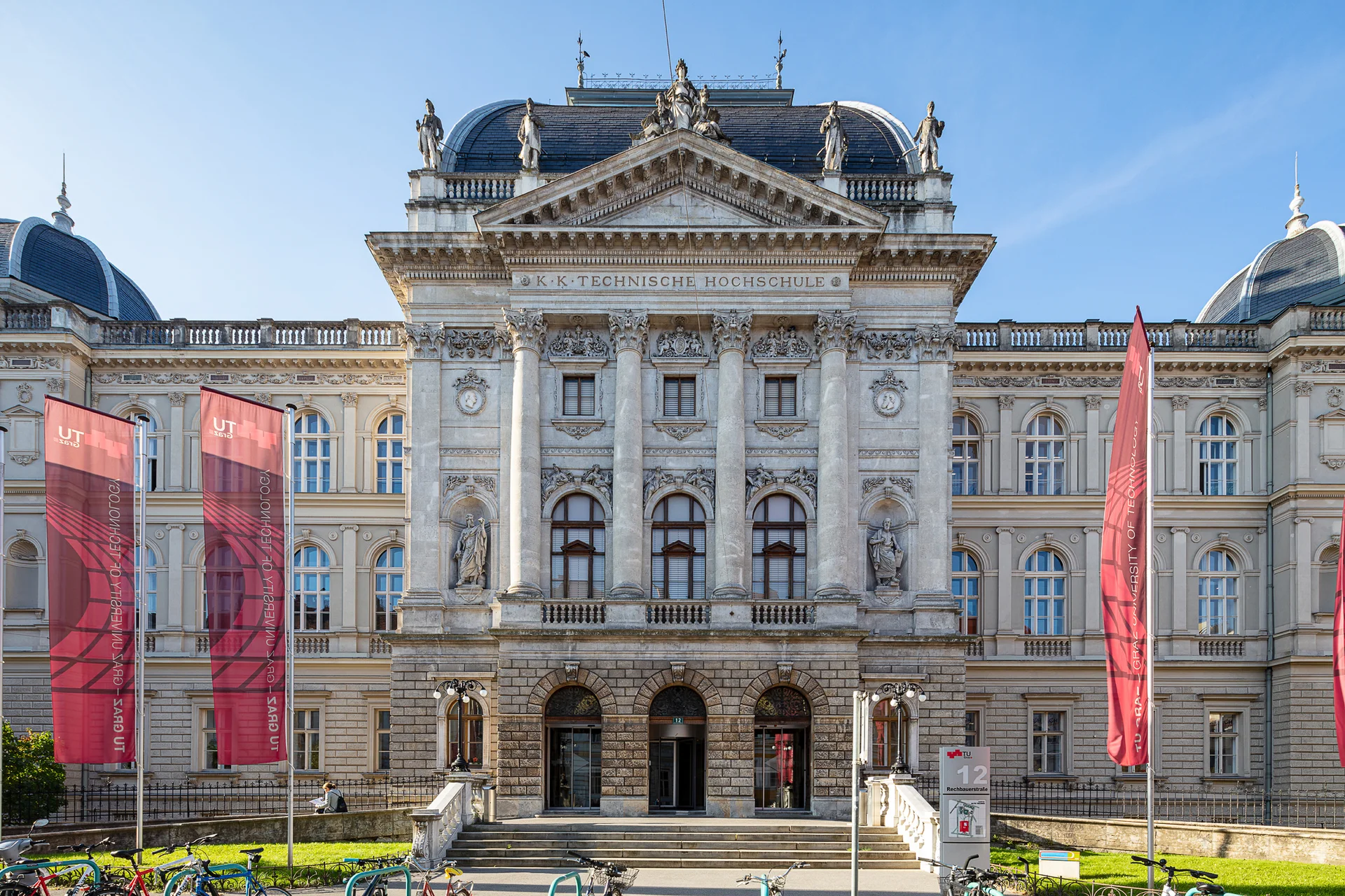 Drei Fahnen wehen an Masten vor einem dreistöckigen, historischen Gebäude.