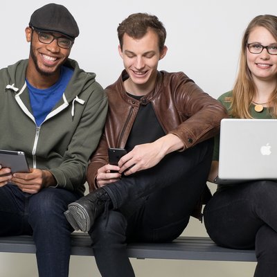 Zwei Studenten und eine Studentin der TU Graz auf einer grauen Bank mit Laptop und Tablet.