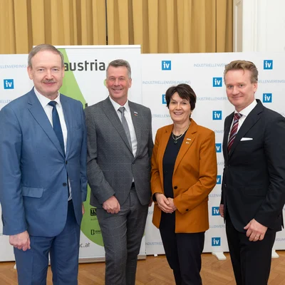 Vier Personen stehen nebeneinander vor einer Logo-Wand.