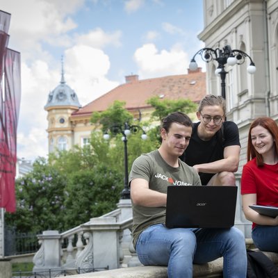 Drei Personen sitzen auf einem Treppenasatz und schauen auf den Bildschirm eines Laptops.