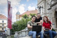 Drei Personen sitzen auf einem Treppenasatz und schauen auf den Bildschirm eines Laptops.