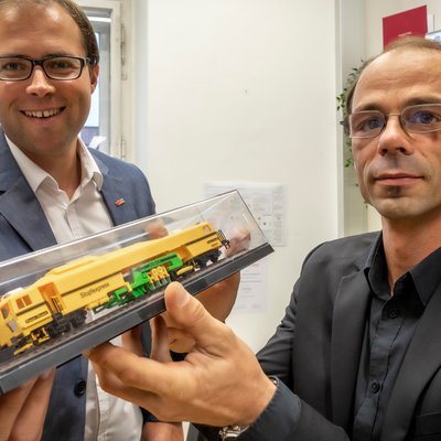 Zwei TU Graz-Forschende mit einem Modell einer Stopfmaschine in Händen