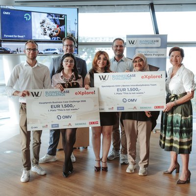 Gruppe von sieben Personen bei einer Preisverleihung an der WU; zwei Teilnehmende halten große Sieger-Schecks der Business Case Challenge mit Partner-Logos wie OMV.