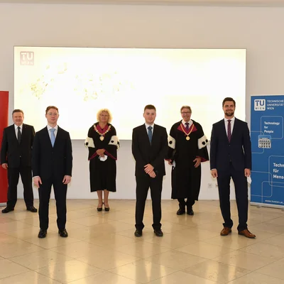 Gruppenfoto der Sub auspiciis Absolvent_innen mit Rektorin Seidler, Vizerektor Matyas und Bürgermeister Ludwig vor TU Wien Logo