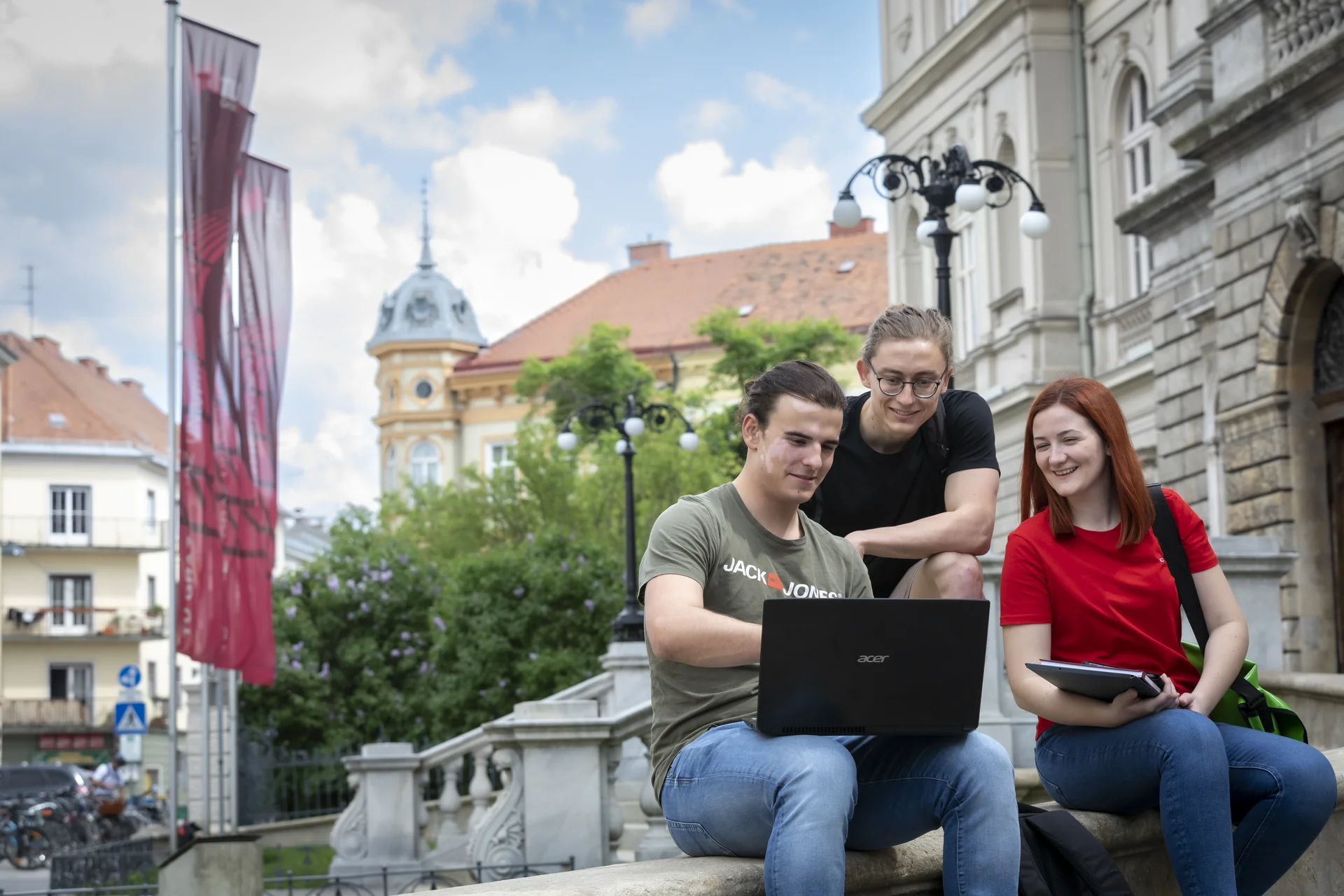 Drei Personen sitzen auf einem Treppenasatz und schauen auf den Bildschirm eines Laptops.