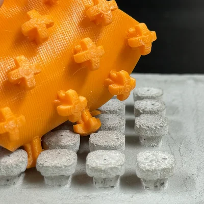 Ein quadratisches, oranges Plastickstück mit Noppen, die sich in ein entsprechendes Gegenstück auf einem Betonteil verhaken.