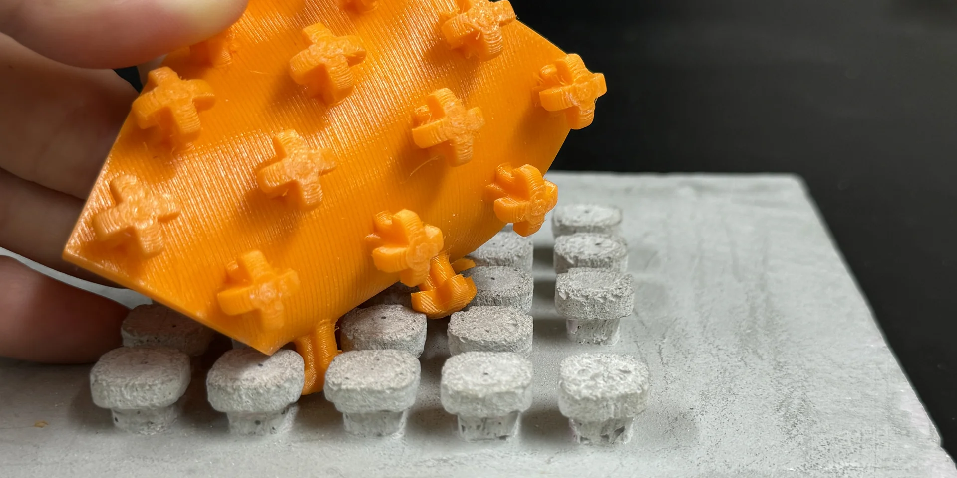 Das Klettelement verhakt sich im Bauteil. Bildquelle: IAT - TU Graz Ein quadratisches, oranges Plastickstück mit Noppen, die sich in ein entsprechendes Gegenstück auf einem Betonteil verhaken.