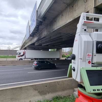 Ein Vermessungsgerät steht vor einer Autobahnbrücke.