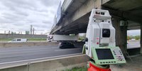 Ein Vermessungsgerät steht vor einer Autobahnbrücke.