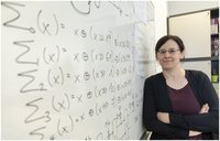 Lächelnde Frau lehnt an Tafel mit mathematischen Symbolen.