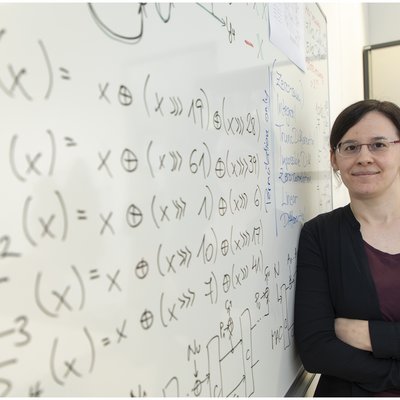 Lächelnde Frau lehnt an Tafel mit mathematischen Symbolen.