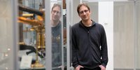 Ein Mann mit schwarzem Pullover steht zwischen Vitrinen. 