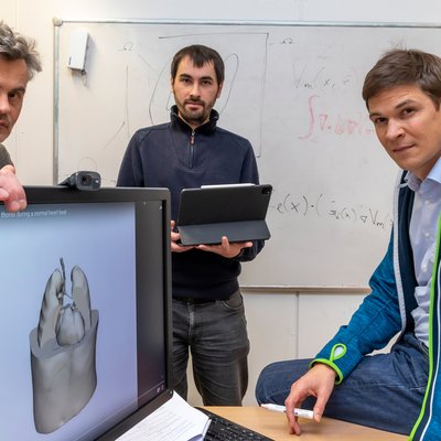 Drei Herren vor einem Computerbildschirm, ein digitales Herz ist abgebildet