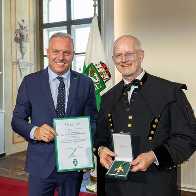 Übergabe einer Landesauszeichnung; Urkunde und Orden werden präsentiert.