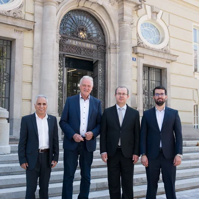 Vier Personen in formeller Kleidung stehen für ein Gruppenfoto vor einem historischen Gebäudeeingang.