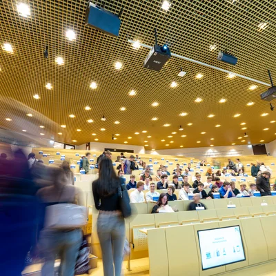 Neue Studierende treffen zur Begrüßungsveranstaltung in einem großen Hörsaal der Montanuniversität Leoben ein; im Vordergrund sind Personen in Bewegung unscharf zu sehen.